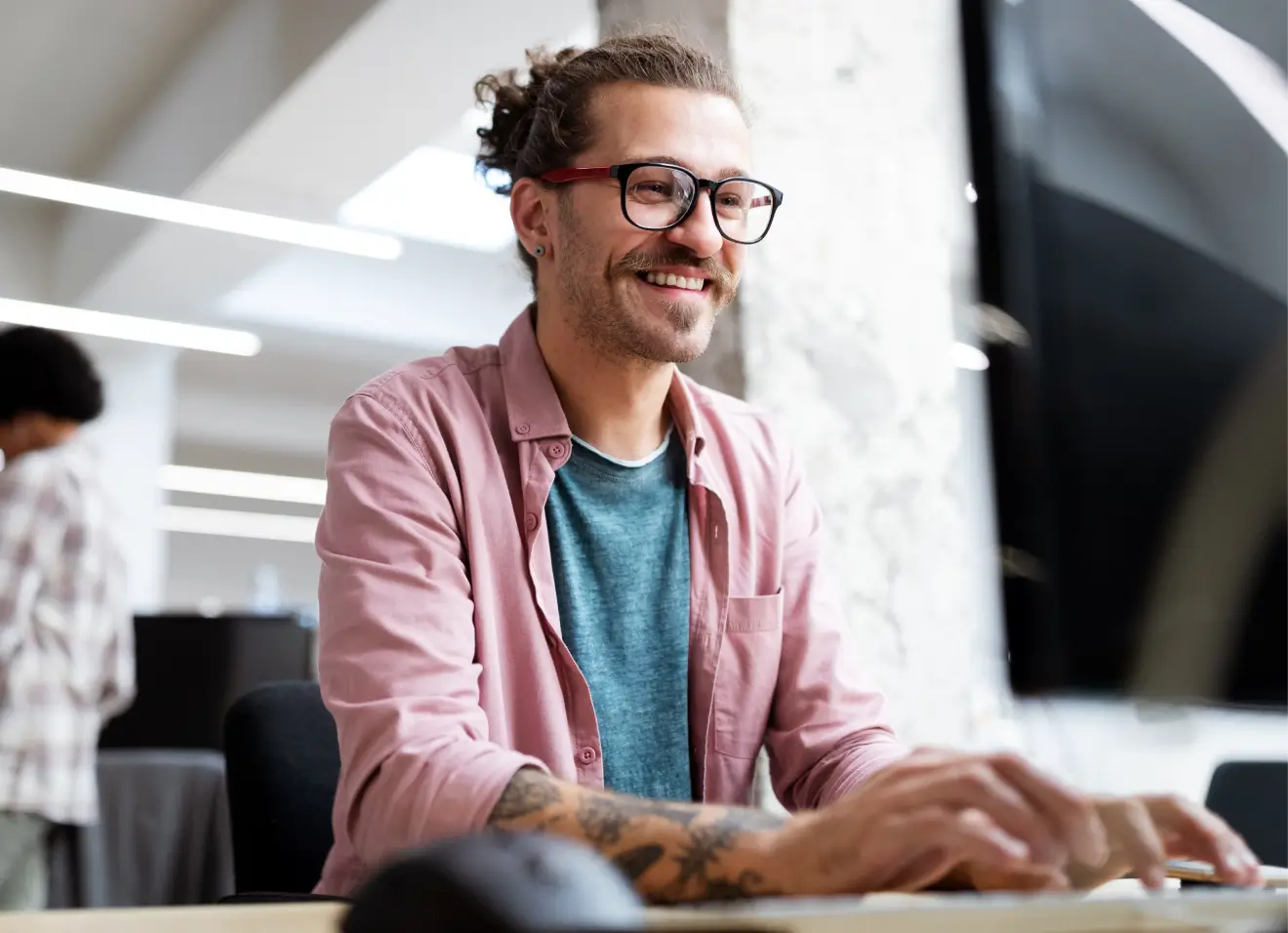 p6-training-online Man wearing glasses working on a computer in a modern office.